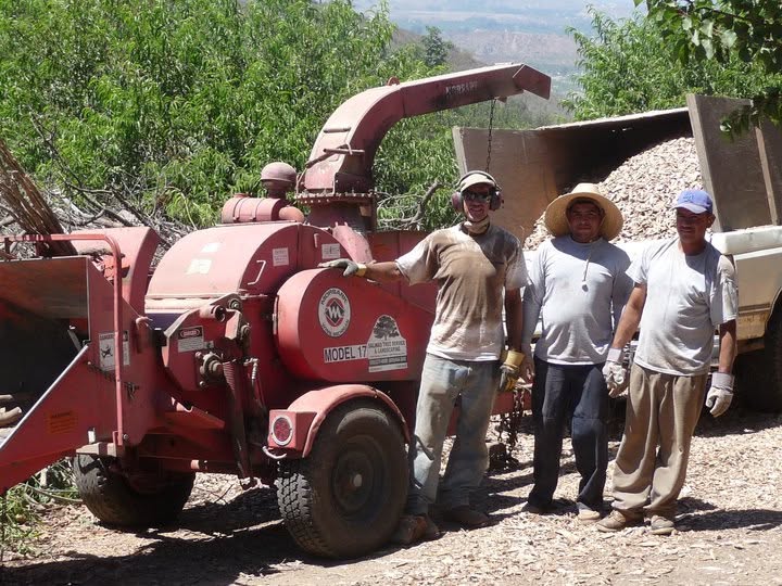 Three crew members beside a red wood chipper and a truck bed full of chips on a Santa Rosa Valley hillside